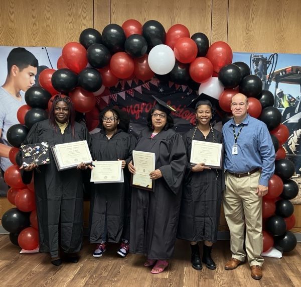 Group of graduates holding their diplomas, and a faculty member standing with baloons and school images behind them.