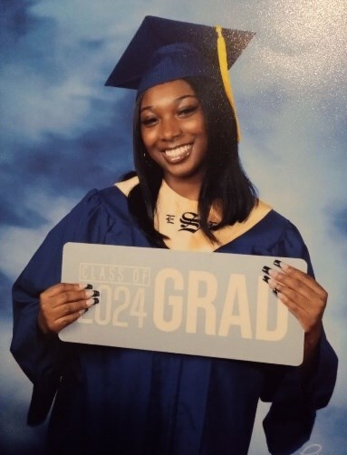 Lucretia McLaughlin - High School Graduate in a cap and gown holding a sign.