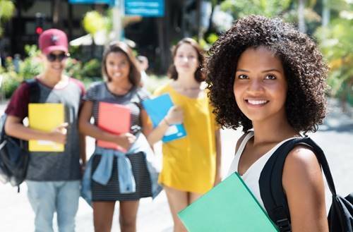 A girl stands with a backpack in front of her three friends.